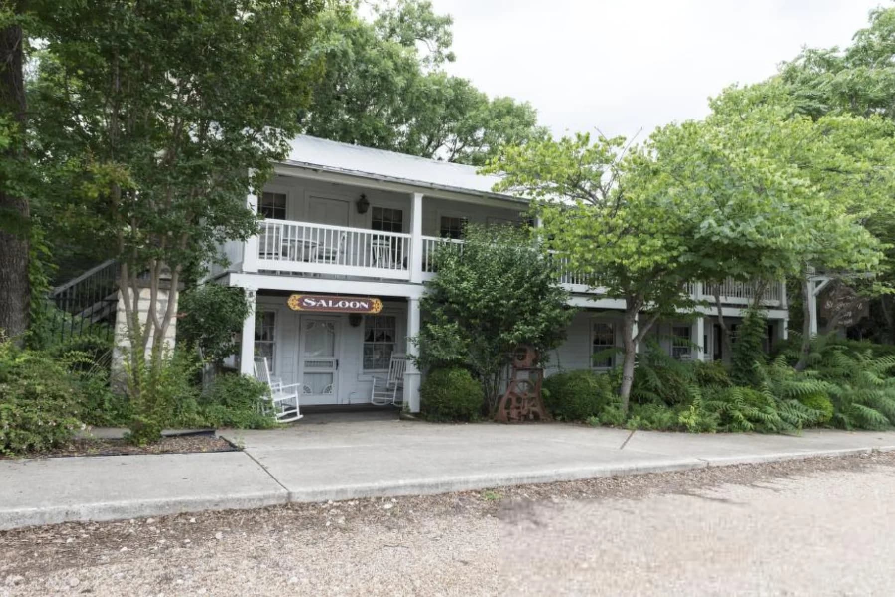 White two-story historic building with a Saloon sign, wraparound porches, and rocking chairs, shaded by trees in Salado, Texas