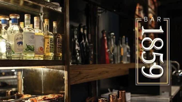 Bar 1859's back bar lined with tequila and mezcal, with the venue's illuminated sign, in Salado, Texas